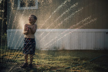 Boy Enjoying Water From Sprinkler While Standing In Backyard