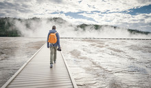 Rear View Of Man Walking On Boardwalk Amidst Lake Against Cloudy Sky