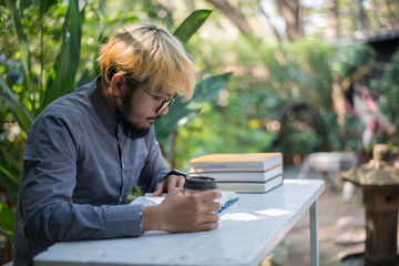 Wall Mural - Young hipster beard man drinking coffee while reading books in home garden with nature. Education concept.