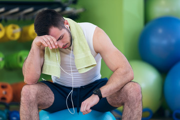 Male athlete kneeling down by dumbbells toweling sweat of his brow.