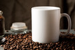 White coffee mug with coffee beans and glass jar with ground coffee inside