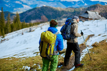 Wall Mural - two hikers with backpack on the trail in the Carpathians mountains at winter. hikers stands on the cloudy sky background