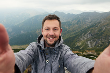 smiling hiker taking a selfie in front of mountain landscape