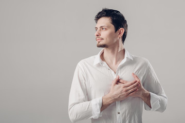 handsome young proud man in shirt holding hand on chest on grey 