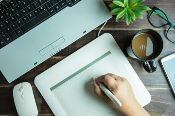 Top view of office stuff graphic design hand drawing on pen mouse pad with laptop mouse and coffee cup on wooden table.Concept graphic design workplace.