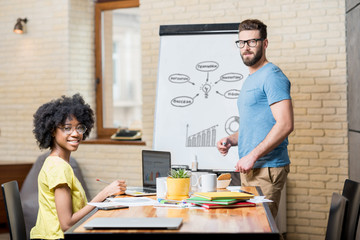 Wall Mural - Multi ethnic coworkers dressed casually in colorful clothes working during the meeting at the office with laptop, documents and whiteboard