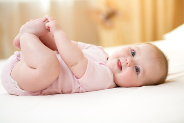 Wall Mural - Funny smiling baby infant girl playing with her feet