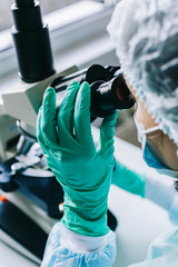Wall Mural - scientist in blue medical gloves and uniform learning samples with microscope in laboratory.