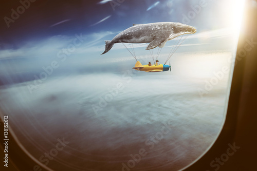 Obraz na plátně Whale floats in the air above the clouds carrying children in a yellow airplane,seen through window of an aircraft , dreams and travel concept