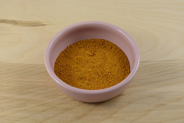 Ground mace spice in pink condiment dish on wooden table