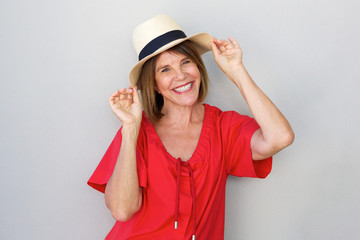 Wall Mural - older woman smiling with hat against gray wall