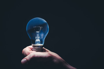 Hand holding light bulb in fingers with blackboard behind.  Concept and idea background.