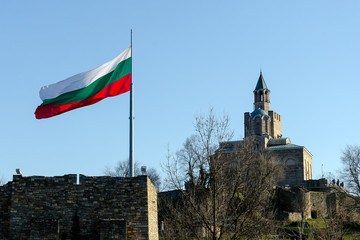 Wall Mural - Waving Bulgarian flag at Tsarevets fortress with patriarch church in background, Veliko Tarnovo, Bulgaria