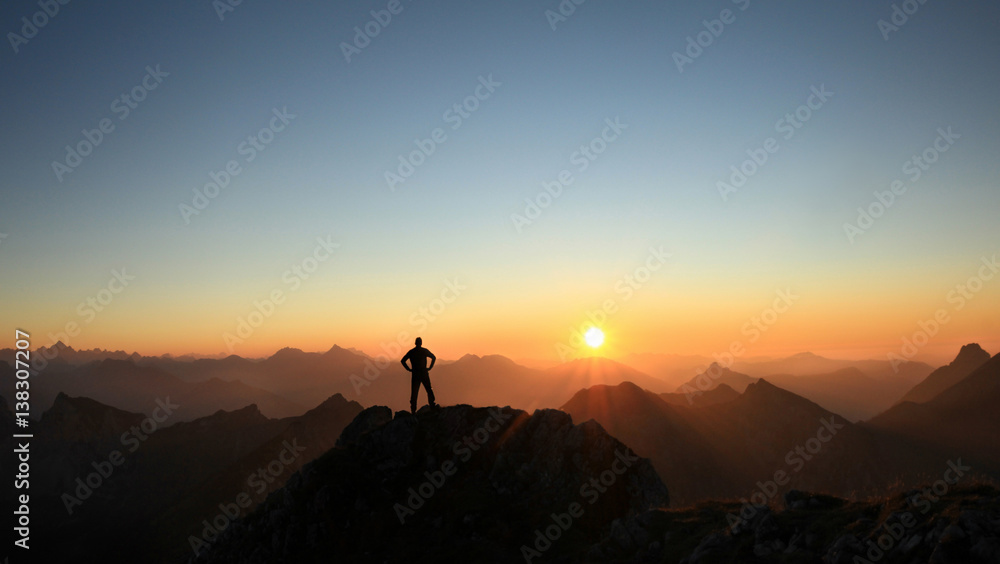 Man reaching summit enjoying freedom and looking towards mountains sunset. - obrazy, fototapety, plakaty 