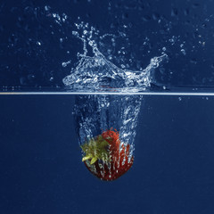 Wall Mural - Fresh juicy strawberry falling in water on blue background