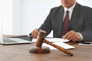 Canvas Print - Brown gavel on wooden table and male lawyer on background, close up view