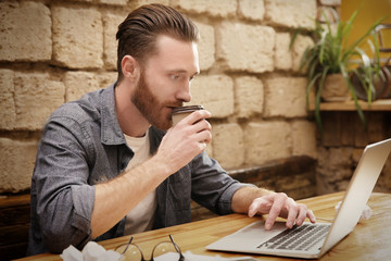 Handsome young man working on computer at cafe