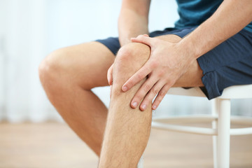Wall Mural - Young man suffering from knee pain at home, closeup