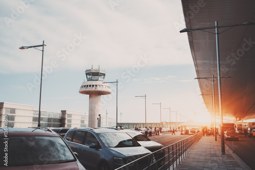 Zdjęcie XXL Parking, droga i taksówka w pobliżu nowoczesnego terminalu lotniska współczesnego przed wieżą kontroli ruchu lotniczego, z wieloma pasażerami i personelem w oddali, Barcelona, ​​Hiszpania