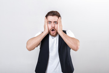 Wall Mural - cute young frightened man with beard in shirt and waistcoat over gray background