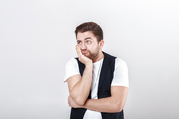 Wall Mural - portrait of handsome pensive brunette man in white shirt on gray background. guy thinks