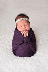 posed newborn girl sleeping in a purple swaddle