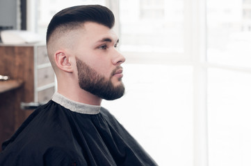 a young guy sitting on a chair in the barbershop. looking to the side