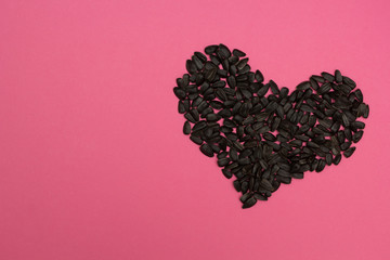 Wall Mural - Heart laid out from sunflower seeds on a pink background.