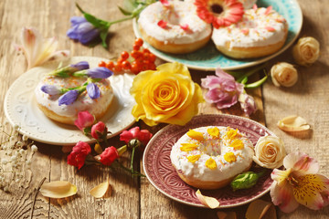 Composition of plates with delicious donuts and colourful flowers on wooden table, closeup