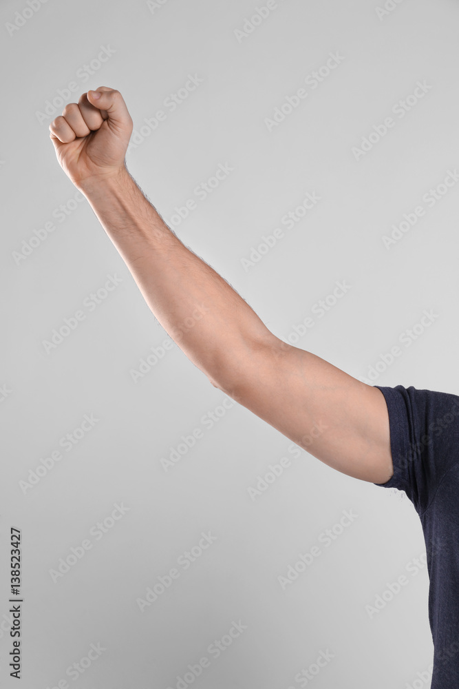 Raised male hand with clenched fist on light background