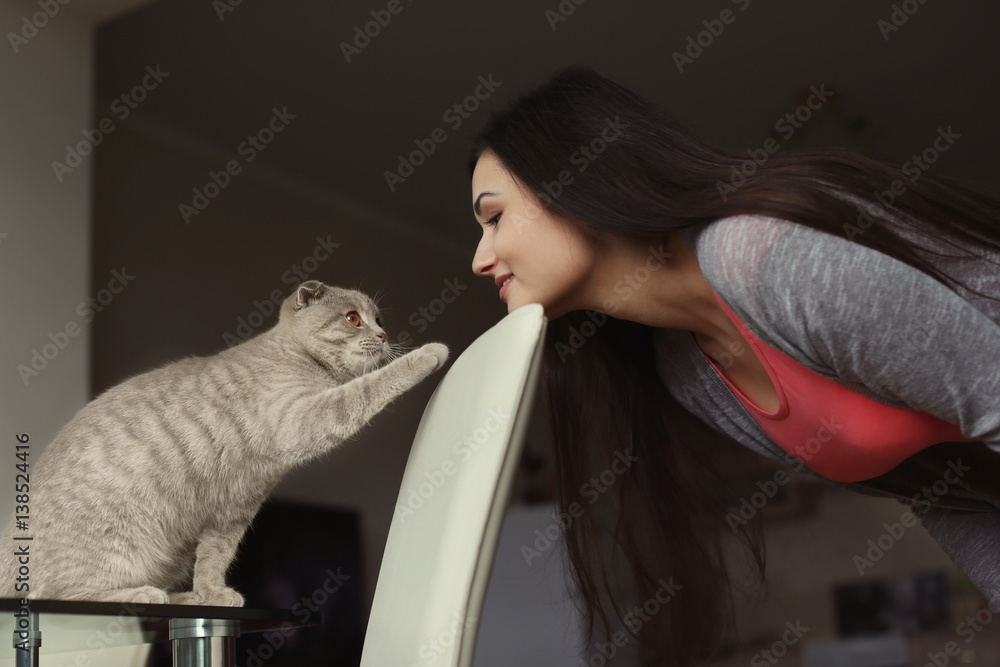 Young beautiful woman playing with cute cat at home