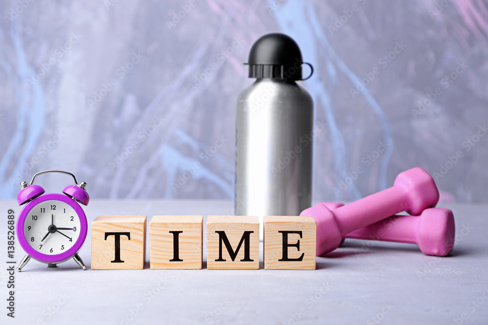 Cubes, alarm clock and dumbbells with bottle on color background. Time concept