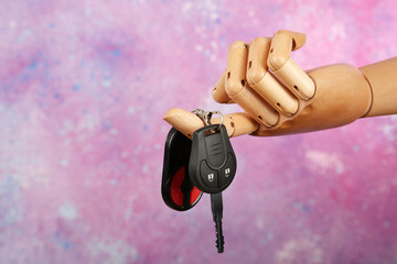 Wooden hand holding car keys on colorful background