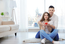 Happy Young Couple With Small Red Heart Sitting On Floor At Home