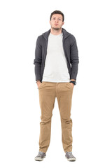 Wall Mural - Casual man wearing zip sweater over white shirt posing with hands in pockets. Full body length portrait isolated over white background.