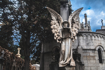 Sculpture of an angel on a cemetery with a roll against the background of leaves