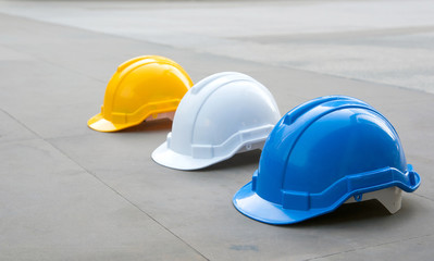 Tree safety plastic helmets : white, yellow and blue on concrete floor at under construction area with copy space. Focus on the blue hat.