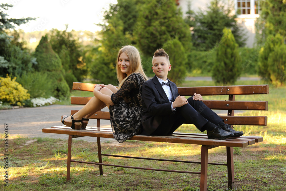 Brat i siostra uśmiechają się, siedząc na ławce w parku. - obrazy, fototapety, plakaty 