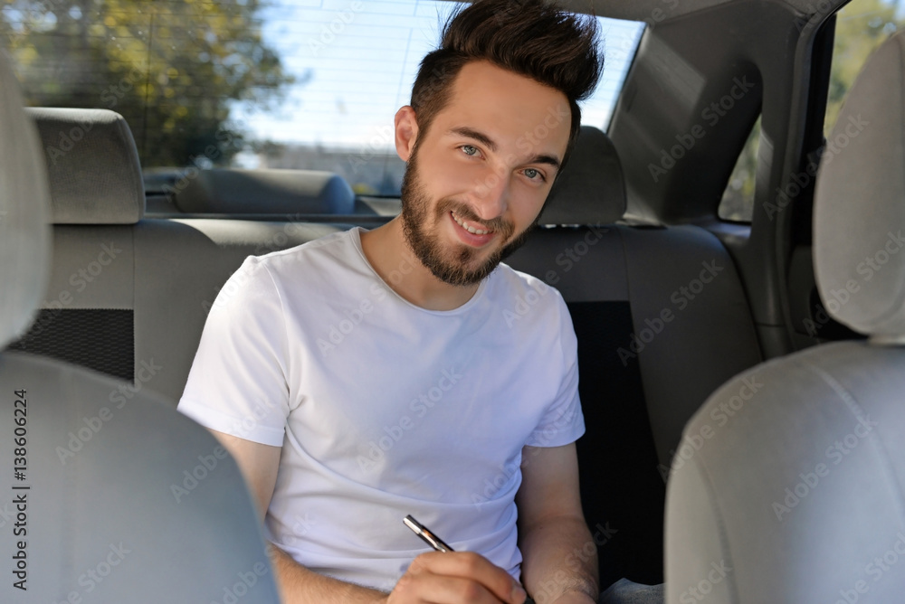 Handsome young man making notes while sitting in car