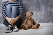 © Africa Studio - Little girl sitting with toy bear on color wall background