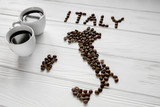 Fototapeta Tematy - Map of the Italy made of roasted coffee beans laying on white wooden textured background with two coffee cups. Space for text