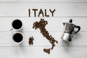 Wall Mural - Map of the Italy made of roasted coffee beans laying on white wooden textured background with two coffee cups and coffee maker. Space for text