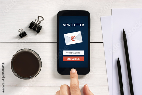 Fotografía Subscribe newsletter concept on smart phone screen with office objects on white wooden table