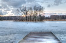Late Winter Landscape. Wooden Pier And Trees Without Leaves On A Frozen Lake.