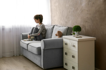 Little girl with toy bear on sofa in room