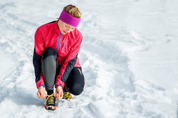 Winter runner getting ready running tying shoe laces. Beautiful fitness model training outside. Copy space on snow.