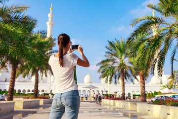 Young tourist woman shooting on mobile phone Sheikh Zayed great white mosque in Abu Dhabi, United Arab Emirates, Persian gulf. UAE is famous tourism destination