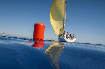 Wall Mural - Sailing boat with yellow spinnaker and red buoy. Calm sea.