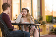 Young couple sitting at an outside table talking, camera focus on the girl.