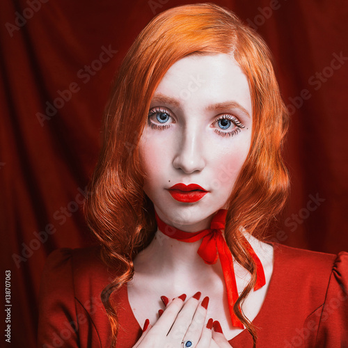 A woman with red curly hair in a red dress and retro makeup